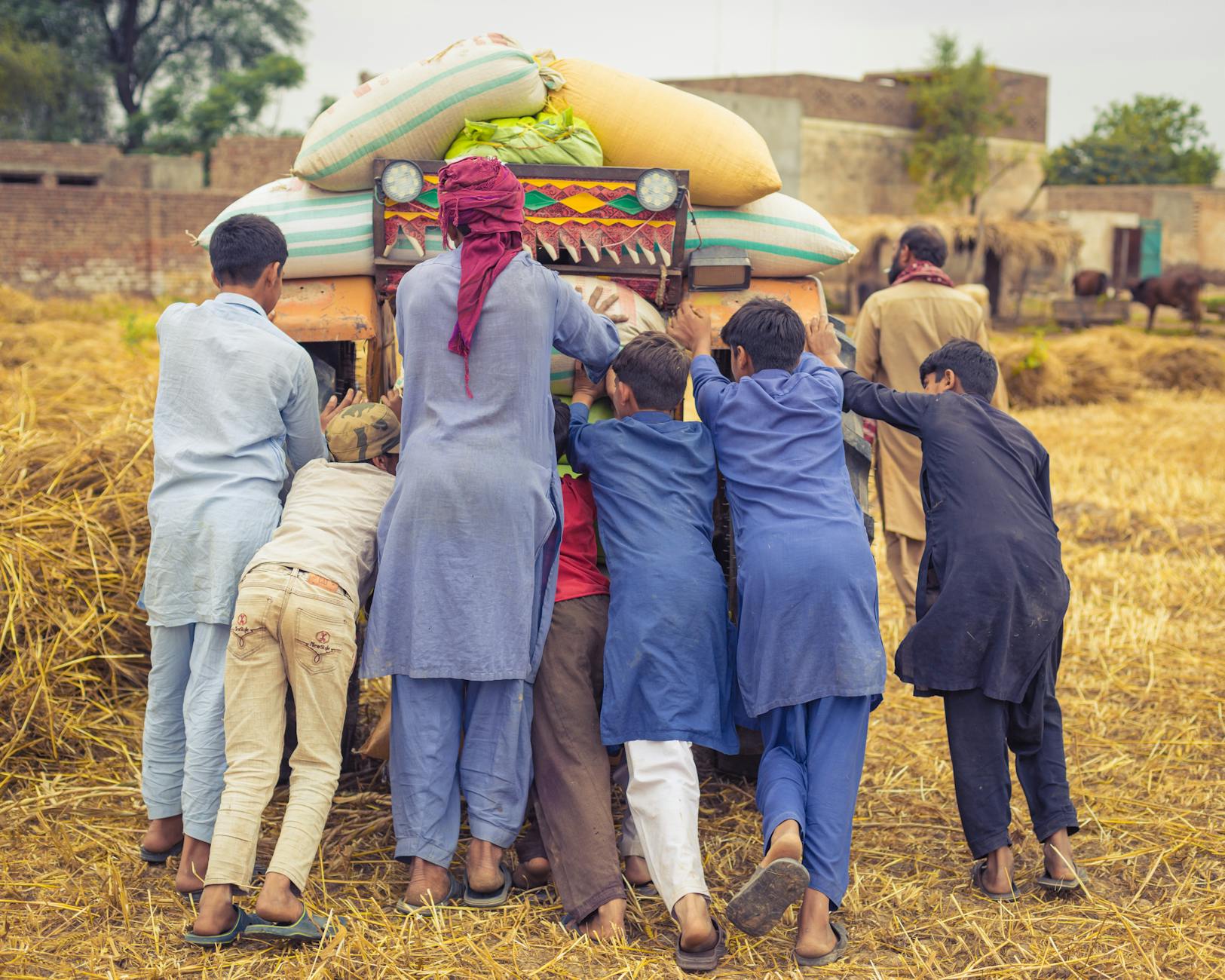 Chłopcy i mężczyźni pchają traktor z sianem na wiejskim podwórku