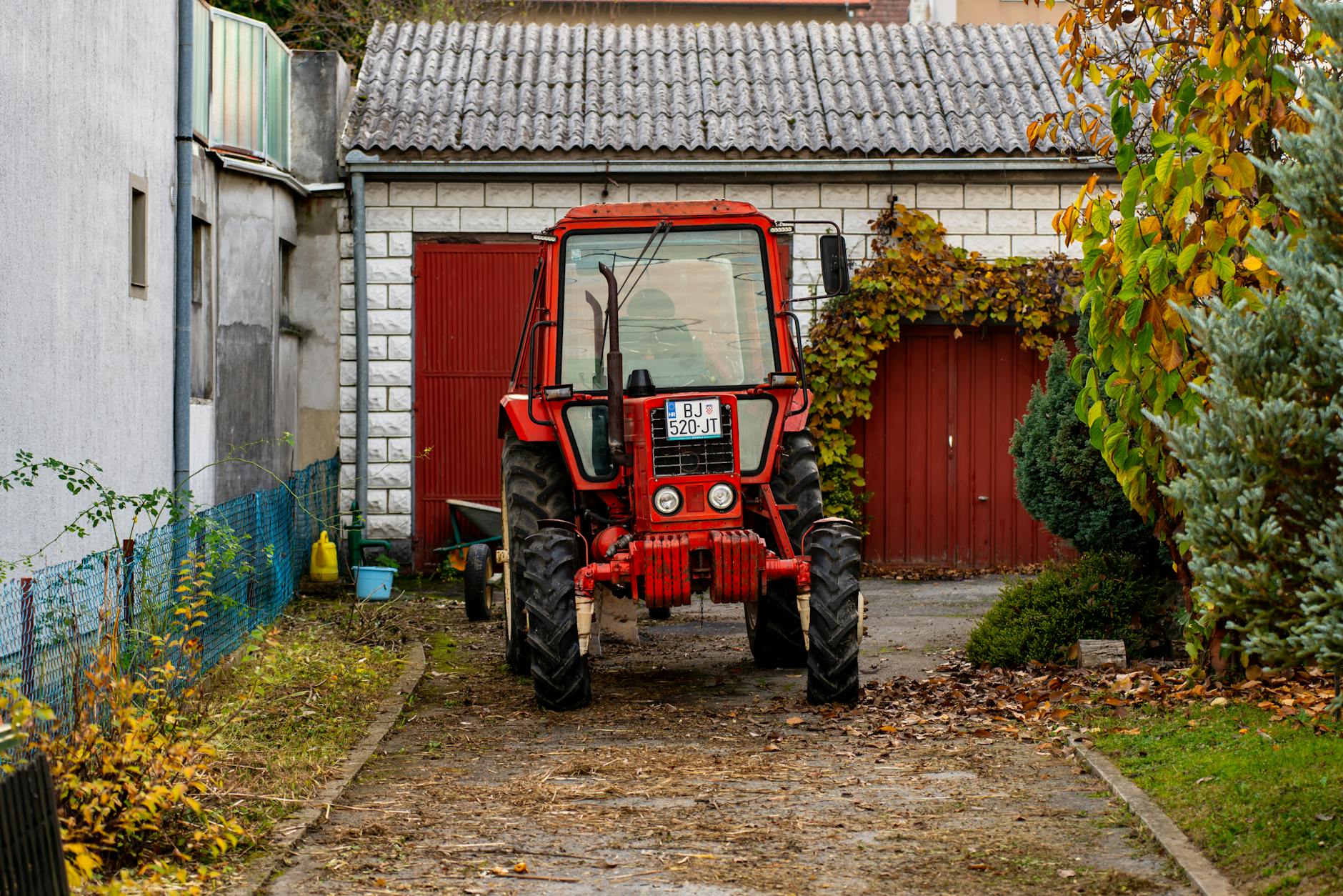Czerwony ciągnik zaparkowany na podwórku małej wiejskiej farmy