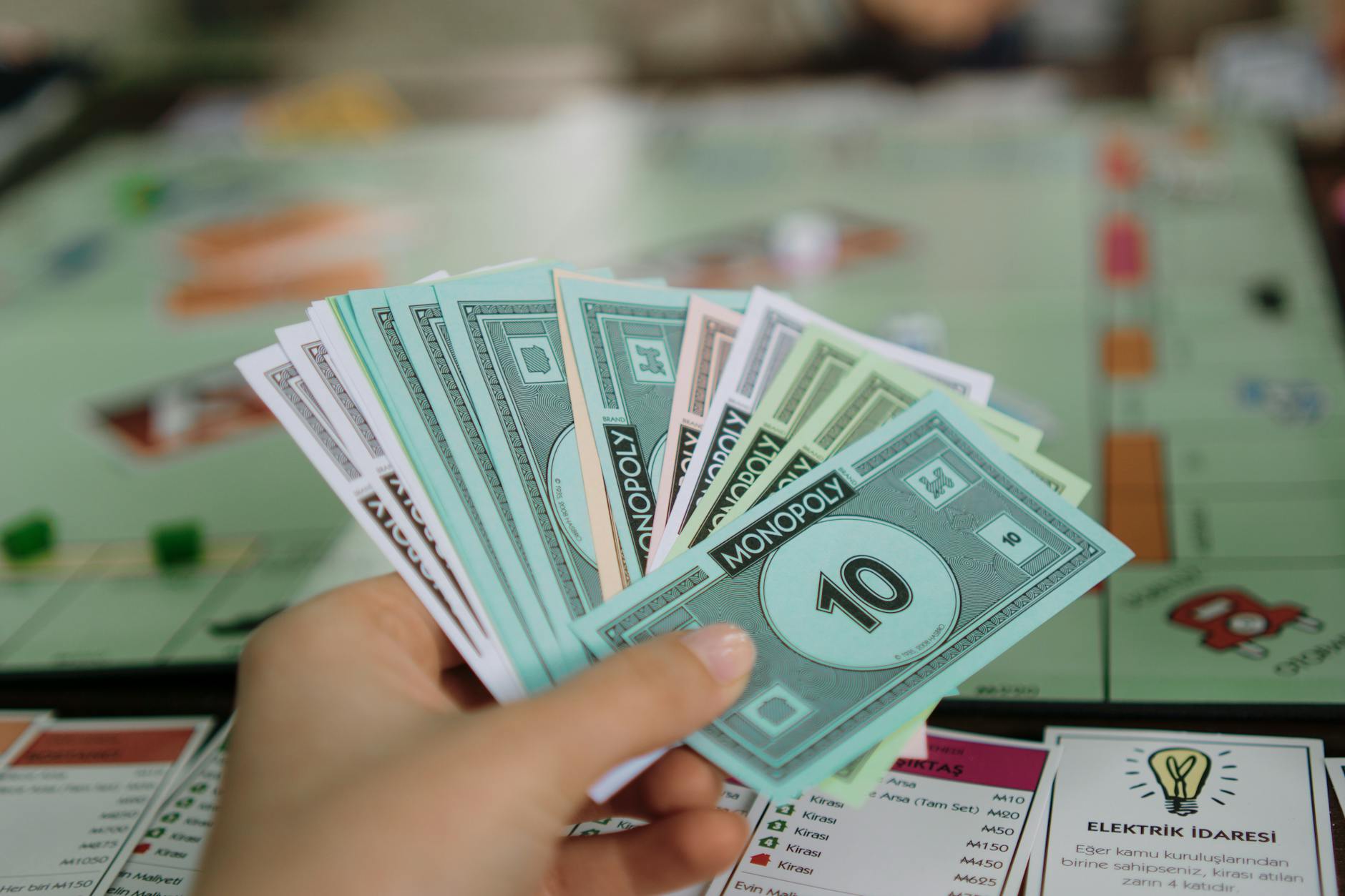 Dłoń trzymająca banknoty Monopoly nad planszą do gry