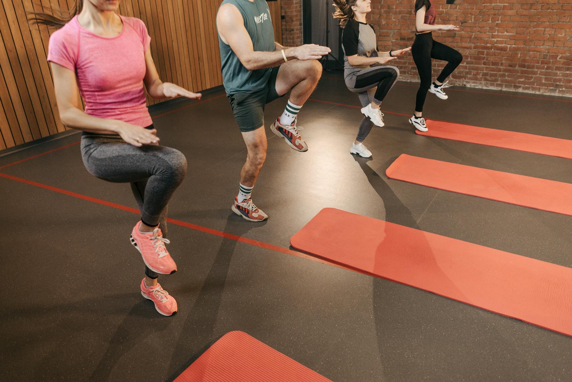 Grupa osób wykonuje wysokie unoszenie kolan na zajęciach fitness w sali