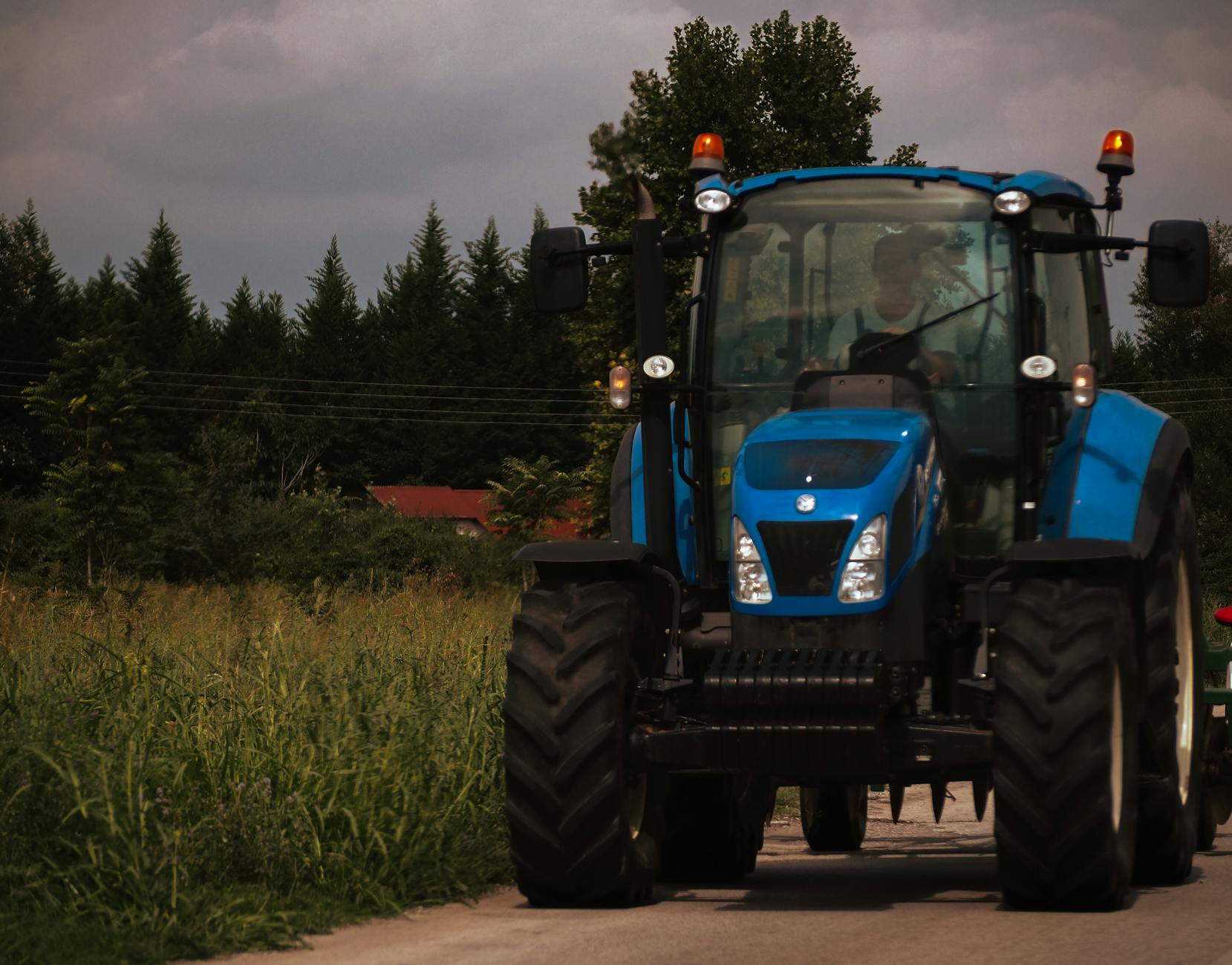 Niebieski traktor jedzie wiejską drogą otoczoną zielenią