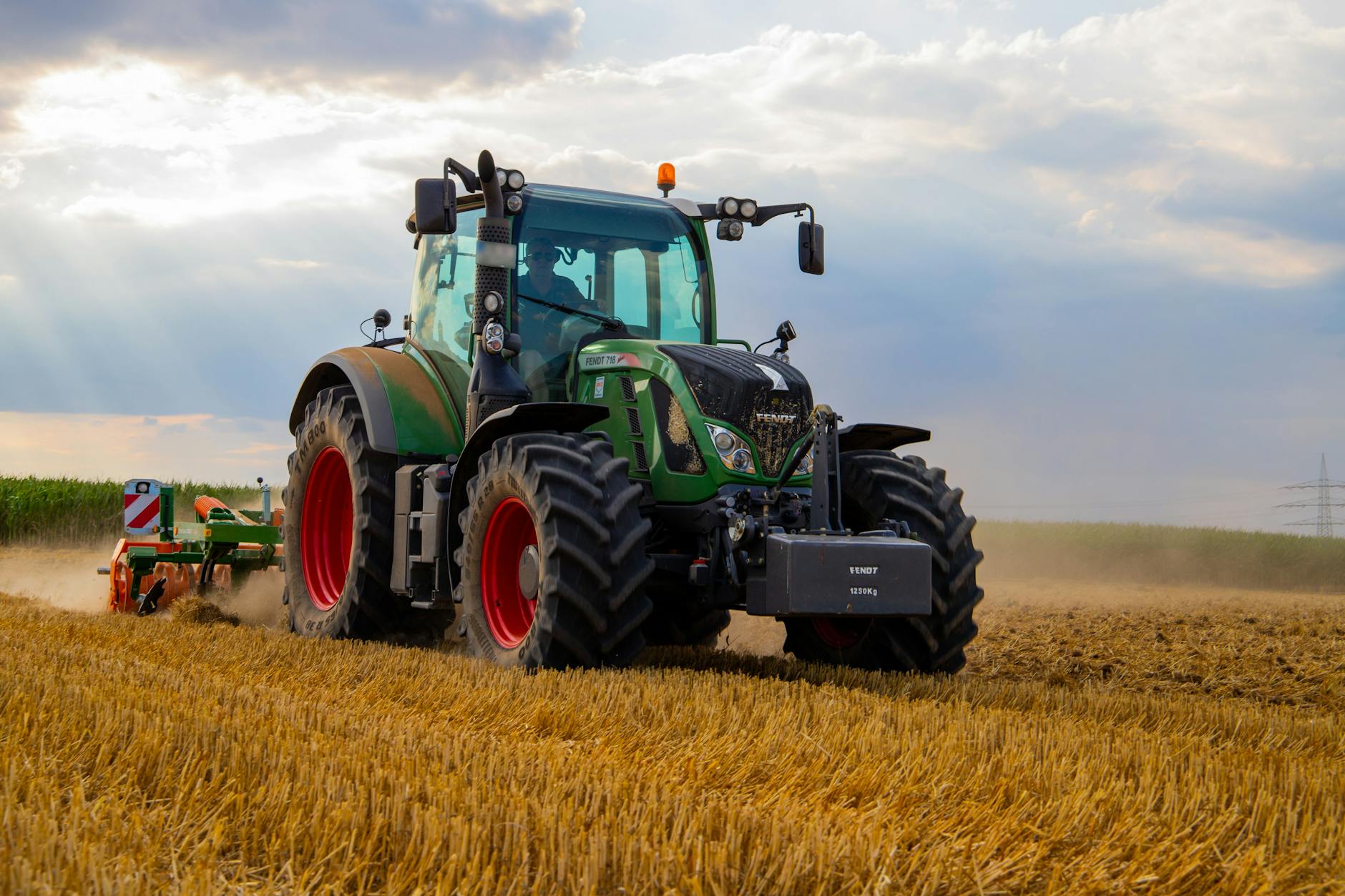 Zielony traktor orze zapylone pole pszenicy pod pochmurnym niebem